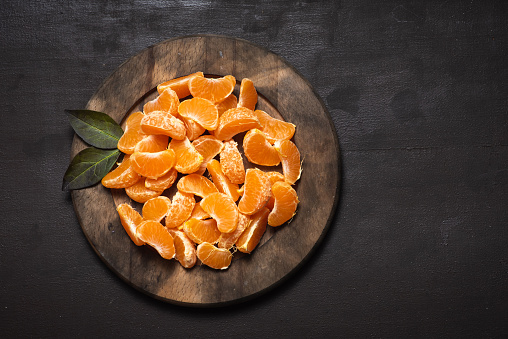 Slice of mandarins served on a round wooden board on a dark wooden background. Top view, with coy space