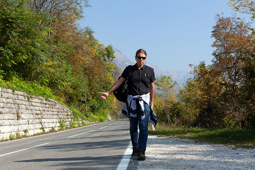 Mid Adult Long Hair Man Backpacker Hitchhiking on a Road in Early Autumn