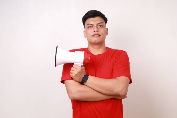 istock Handsome Asian young man standing with folded hands while holding megaphone. Isolated on white 1878582985