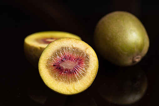 Whole and halved fresh red kiwi fruit on dark glass table, with reflection