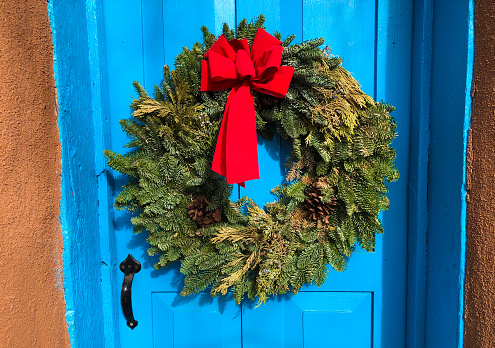 Green Christmas Wreath, Red Bow, Sunlit Blue Door. Shot in Santa Fe, NM.