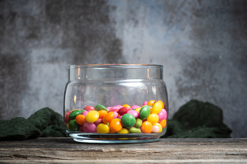 Colorful fruit candies in a glass jar on a gray background