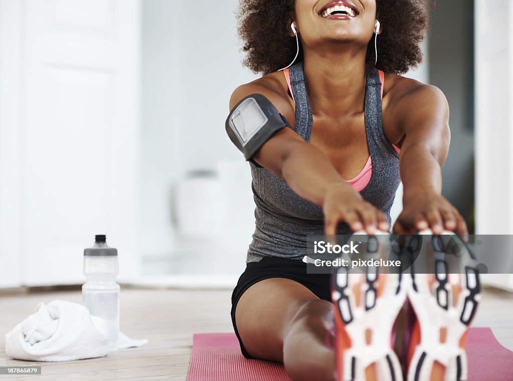 Getting ready to do my workout A fit smiling african american woman in gym clothing sitting on an exercise mat on her living room floor and stretching out her legs with copyspace Home Workout Stock Photo