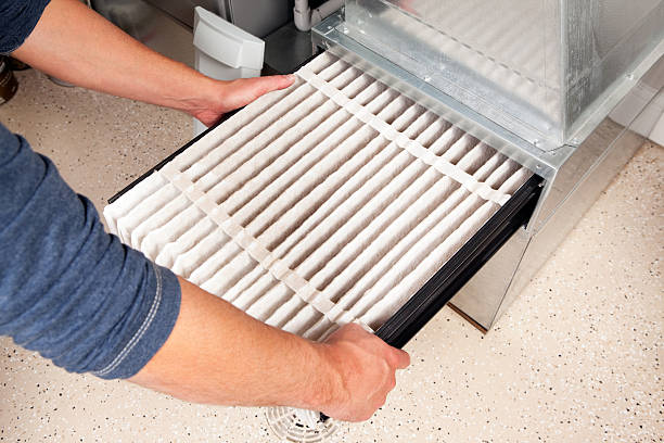 Hands Changing Furnace Air Filter Male hands are installing a furnace air filter. This filter is not brand new but it is relatively clean, it was removed for inspection. This would be a typical filter style found in a high end newer house. The floor is epoxy painted concrete with traction chips and a floor drain. furnace photos stock pictures, royalty-free photos & images