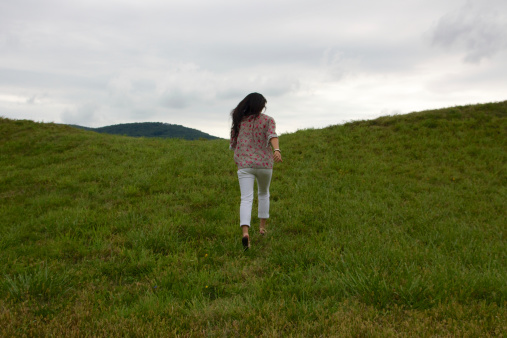 Girl running away from the camera up lush green hills.