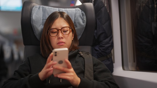 An Asian woman is using her mobile smart phone while traveling by train.