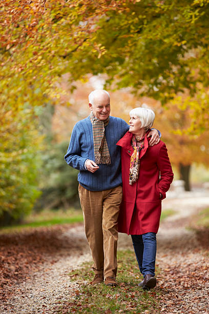 senior pareja caminando por la ruta del otoño - autumn women leaf scarf fotografías e imágenes de stock