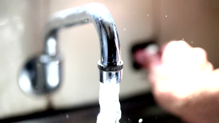 A person is installing a new water-saving faucet in a modern kitchen sink, tools scattered around, highlighting a DIY approach