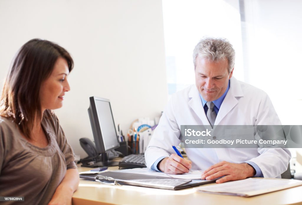 Checking on her medical history A mature doctor sitting behind his desk going through test results with his female patient Doctor Stock Photo