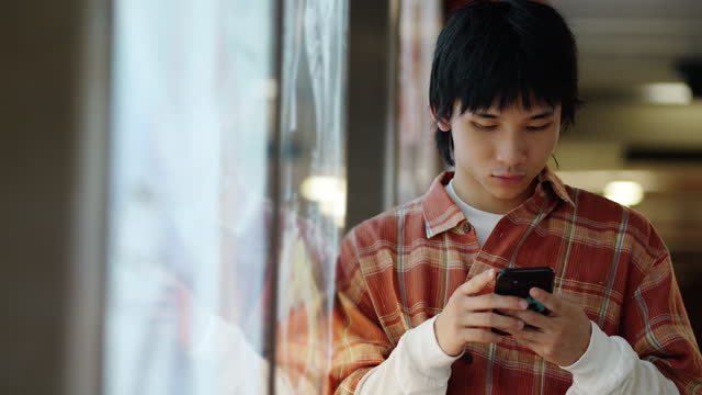Asian Chinese young man leaning on signboard text messaging in subway station