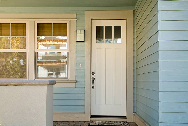 Closed white front door of a house during daytime with blue siding and windows.