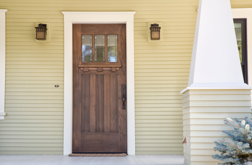 Closed wooden door of a home with yellow siding in daytime.