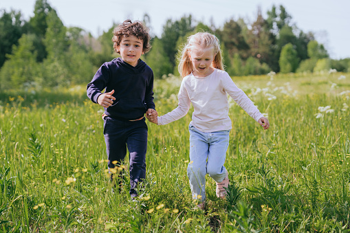 Boy and girl joyfully holding hands and running through a sunny meadow filled with wildflowers, exuding happiness and freedom
