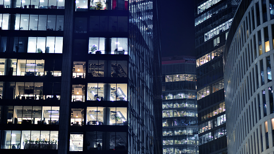 Big glowing windows in modern offices buildings at night. In rows of windows light shines.