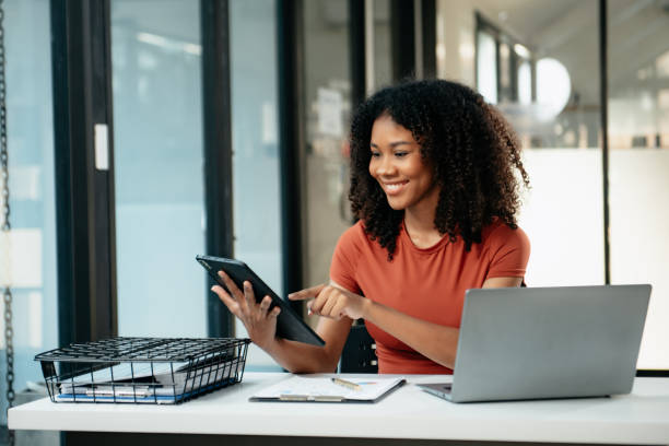 istock Young woman typing on tablet and laptop while sitting at the working in office 1879074092