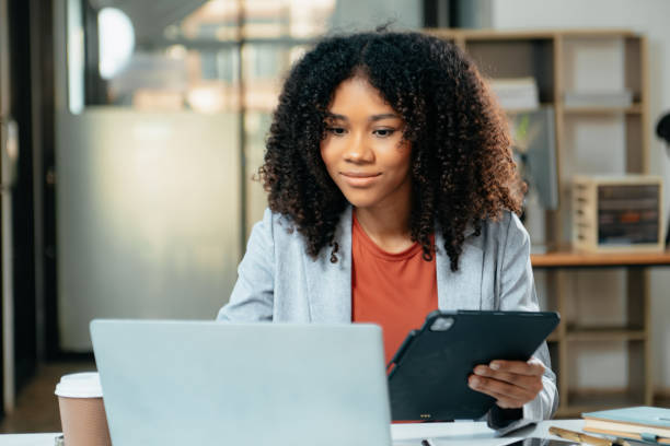 istock Young woman typing on tablet and laptop while sitting at the working in office 1879074629