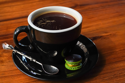 Hot Black Coffee in a porcelain glass on a wooden table. Morning coffee in ceramic mug with macaron and tea spoon. Concept for breakfast, working, task, job, business plan - High angle photo