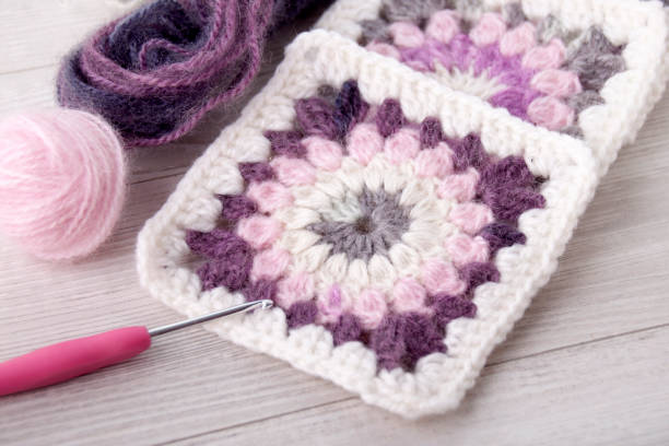 Handmade crocheting granny square, a hook and yarn balls. stock photo