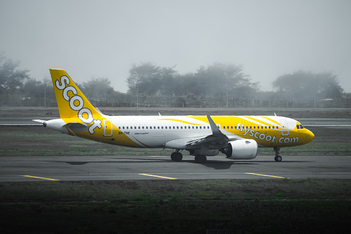 Yogyakarta, Indonesia - October 18, 2023: The Scoot plane is on its way to take off from the airport. Yellow colored airline company plane. The plane take off in foggy weather.