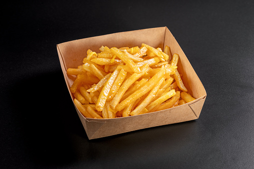 French fries with melted cheddar cheese on top on a black background, in a delivery container.