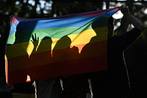 Backlit and Rear view photograph of a silhouette of A group of university student activists raising the rainbow flag campaign for gender equality.