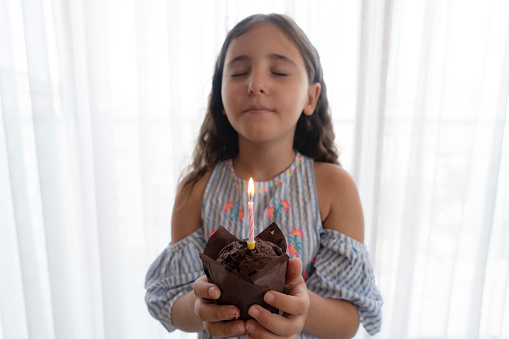 Little girl holding a chocolate muffin with one candle burning