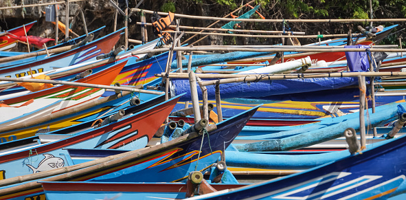 Yogyakarta, Indonesia - August 23, 2023: Many Fisherman fishing boats parked at the shore during sunny day with cliffs rocks backgrounds at Ngrenehan Beach, Gunungkidul, Yogyakarta.