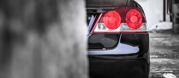 Panorama photo of back of shiny black car with the red light on. Luxury car rear taillights with Empty blank copy text space and blurred bokeh background for banner.