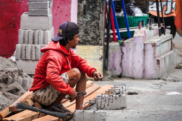 Yogyakarta, Indonesia - August 31, 2023: Craftsmen or handyman are assembling iron for the building foundation frame. An Indonesian man working on construction site during the day.