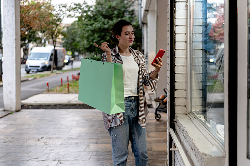 A young woman impressively juggles her window shopping excursion while staying connected on her mobile phone