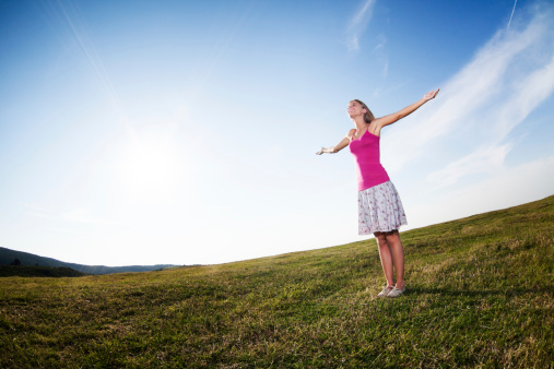 Cheerful woman hiking stands arms outstretched in the valley, welcoming the sun rising on the mountains.