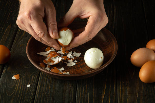 istock A cook peels a boiled egg from its shell on the kitchen table with his hands. Healthy eggs white diet concept. Advertising space. 1879304875