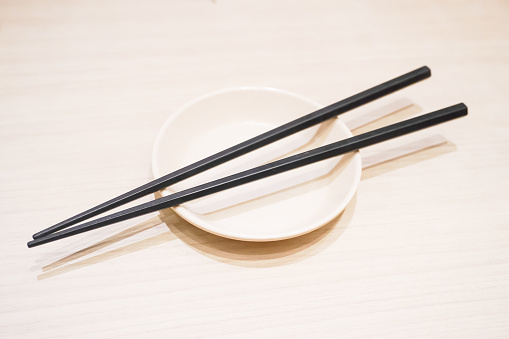 Top view of black wooden chopsticks on small white plate and table blackground. Japanese, Chinese, East Asian Oriental tableware concept.