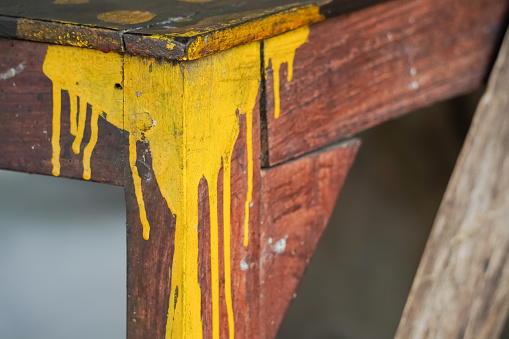 Yellow colored paint drips on the corner of wooden table due to errors and failures in painting. Bad unskilled and careless craftsman or painter. Blank empty copy text space.