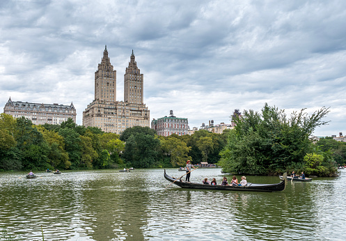 Central Park Lake and West Side skyline, New York City. People rowing on the lake. One Italian gondola visible.