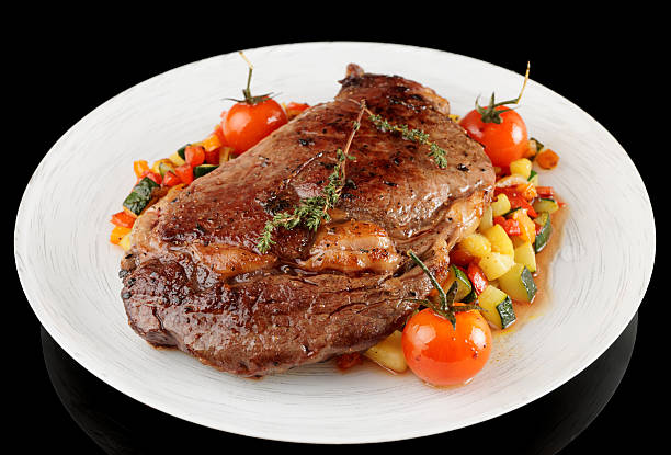 istock Ribeye steak with stir fried vegetables isolated on black 187934325