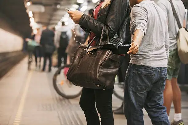 Thief stealing wallet from purse of a woman using mobile phone at the subway station. Pickpocketing at subway station