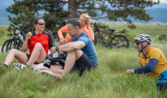 Mature couples talking and relaxing on grassy hill while doing mountain biking.  Healthy lifestyle concept