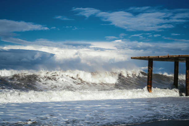 Close-up of ocean waves splashing against weathered wooden posts on a sandy beach, capturing dynamic water motion and spray.