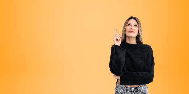 istock Smiling young woman with finger pointing up, copy space background 1879435284