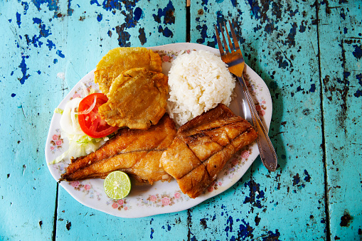 Looking down on a meal of grilled fish, rice and plantains - resting on a rustic colourful table top