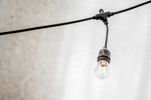Hanging lightbulbs connected by a cable with white background. Close-up light chain decoration with shady bright background. Festive lights garland. light bulbs on string wire.