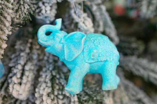 A glittering blue elephant ornament hangs amidst frosted branches, a whimsical addition to festive decor.