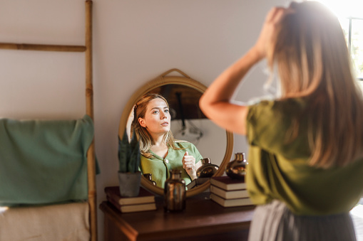 Selective focus shot of happy mid adult woman enjoying looking in the mirror, examining her hair and skin health.