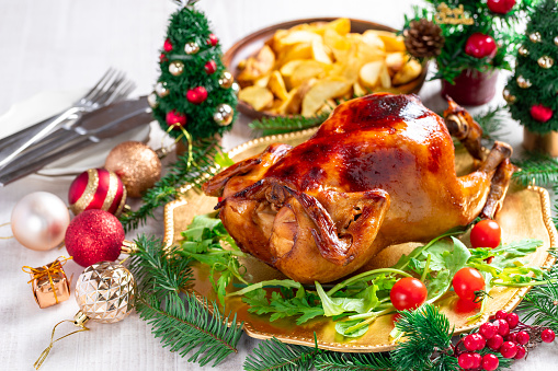 Roasted whole chicken with Christmas decoration. White wooden background.