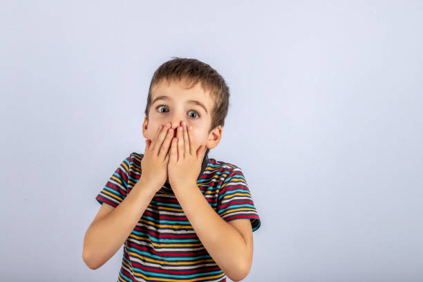 istock boy covers his mouth with two hands from fright on a blue background 1879557085