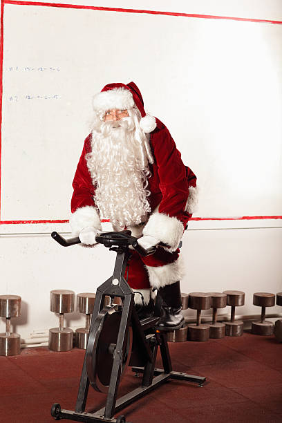 papai noel treinamento na bicicleta ergométrica na academia de ginástica - pedal bicycle sports training cycling - fotografias e filmes do acervo