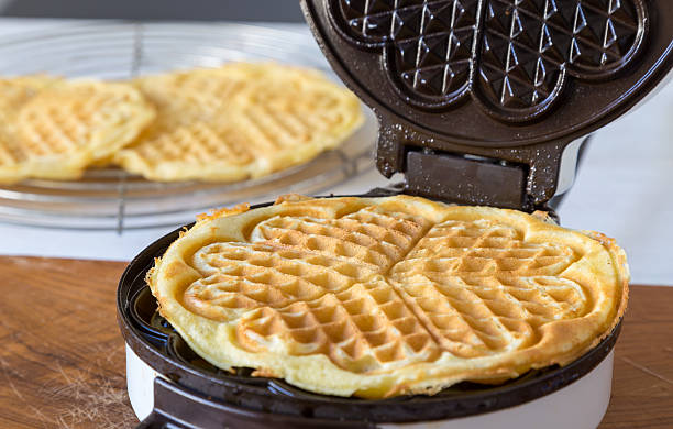 Heart shaped waffle maker in use on a wood countertop stock photo