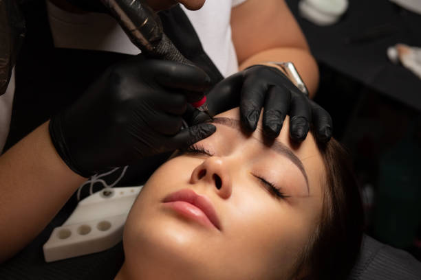 istock Beautician doing eyebrow permanent makeup on woman face 1879578298