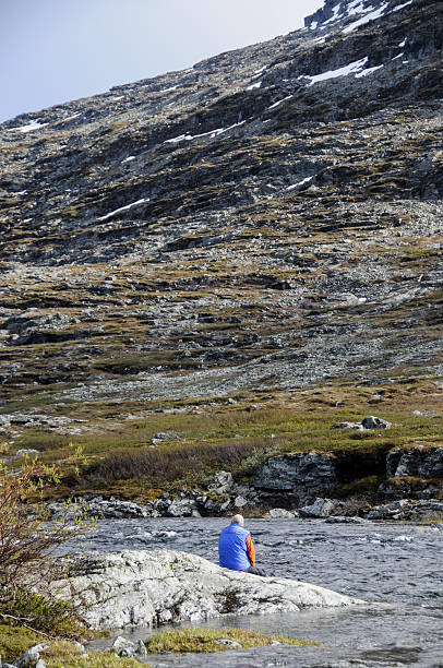 istock Man sitting by river in wilderness with mountains 187961258
